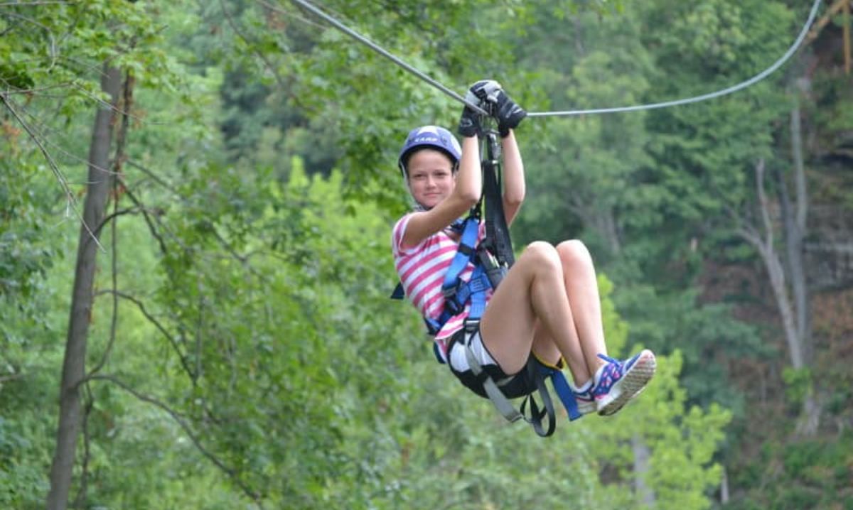 A young girl enjoying a thrilling zipline ride through the lush green forests of Hocking Hills, Ohio, during an outdoor adventure experience.