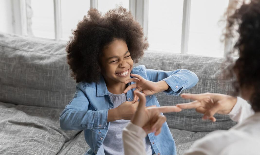 A joyful child with autism communicates using sign language with a caregiver on a couch. The image highlights the importance of nonverbal communication methods and supportive interactions for children with autism.
