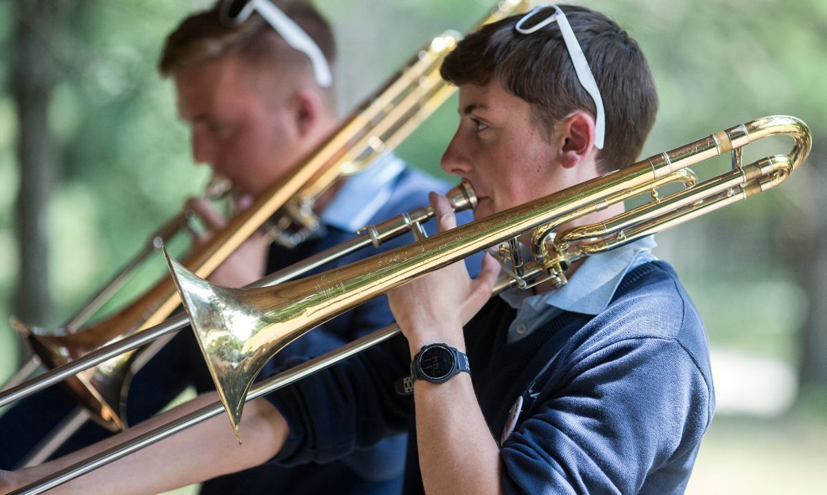 Two young trombone players in Blue Lake Fine Arts Camp uniforms performing outdoors, wearing sunglasses on their heads.