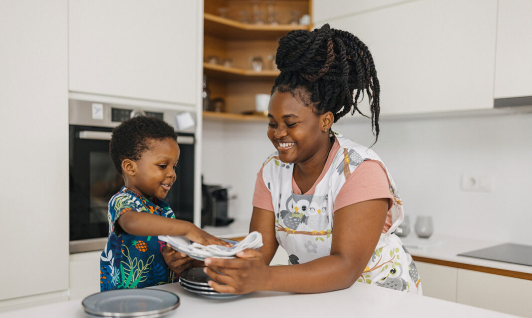 A smiling mother and her young child work together to put away dishes in a bright, organized kitchen. Practicing mindfulness and daily routines can help declutter your mind and create a sense of calm.