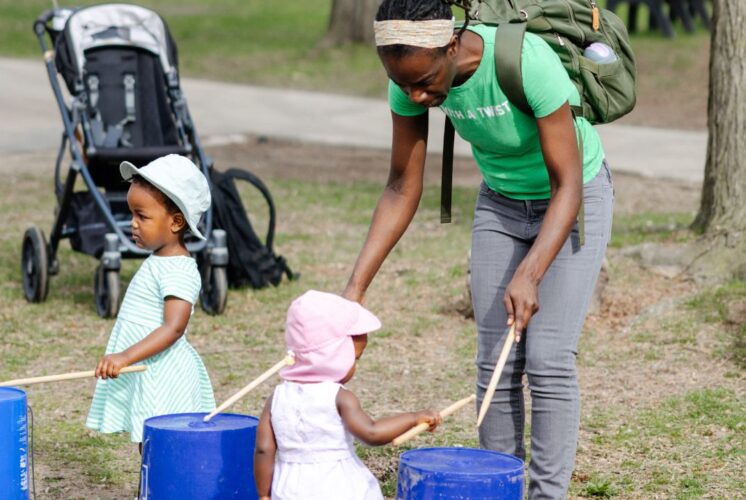 Young children and parent enjoying a hands-on drumming activity at GreenFest at the Detroit Zoo, a family-friendly outdoor spring event