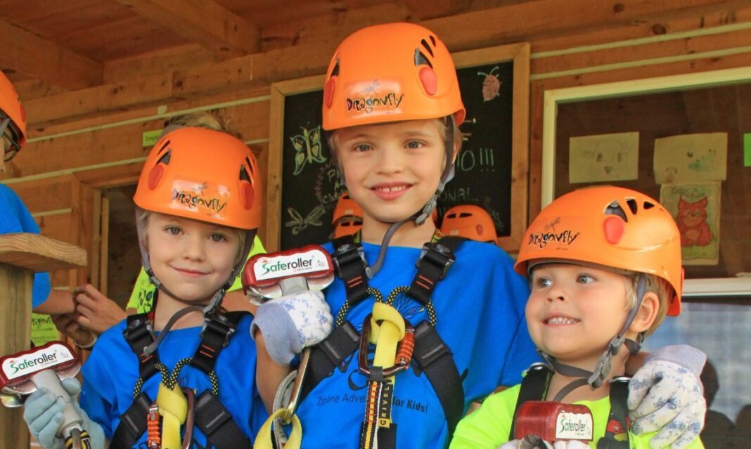 Three young children wearing helmets and harnesses, excitedly preparing for a zipline adventure at Hocking Hills Zipline Adventures, a popular outdoor activity for families in Ohio.