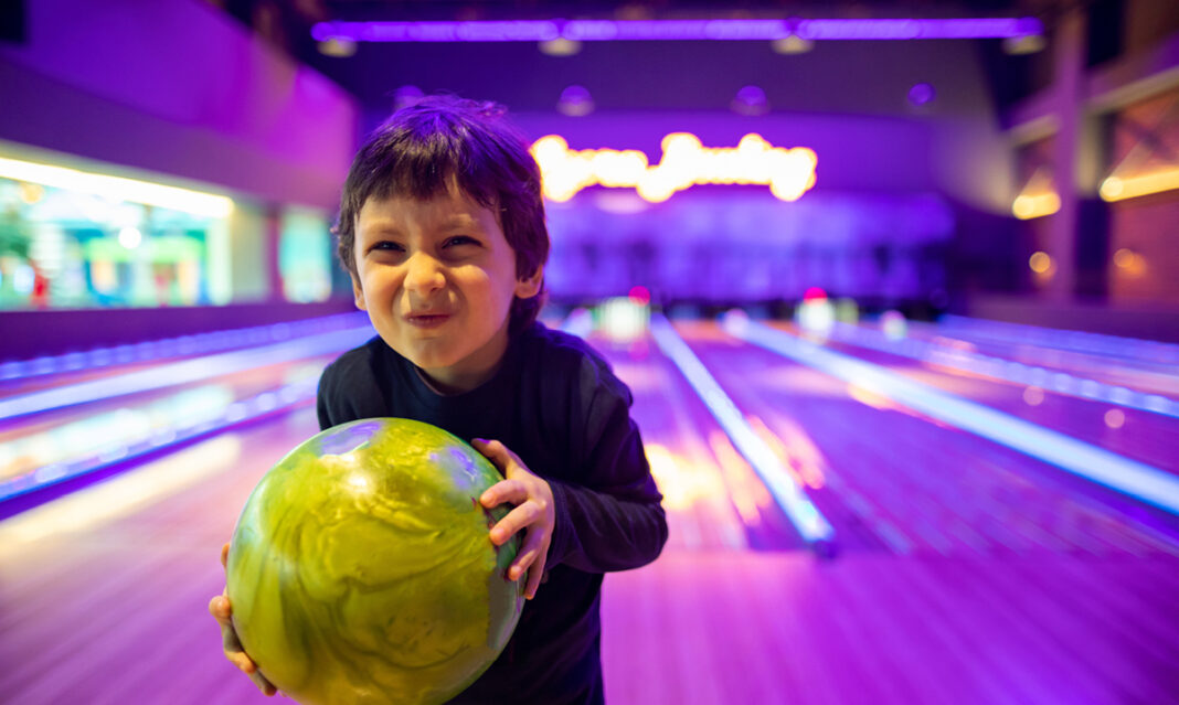 Smiling young child holding a bright green bowling ball at a glowing kid-friendly bowling alley in Metro Detroit.