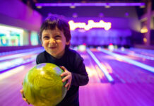 Smiling young child holding a bright green bowling ball at a glowing kid-friendly bowling alley in Metro Detroit.