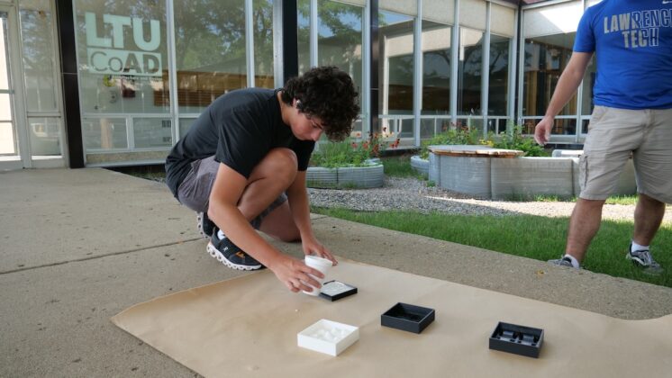 A student participates in an architecture workshop at Lawrence Tech summer programs, working on a hands-on design project outside the College of Architecture and Design building.