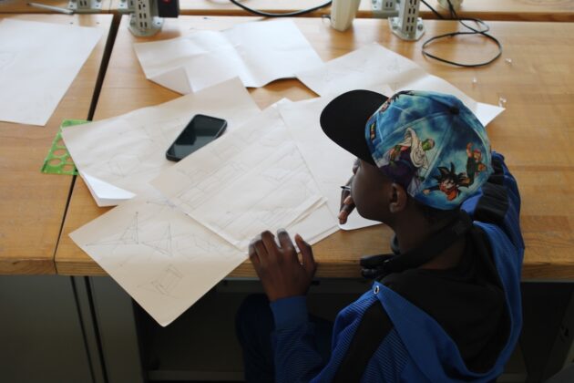 A student participates in a design workshop at Lawrence Tech summer programs, sketching architectural and engineering concepts at a workspace filled with drawings and tools.