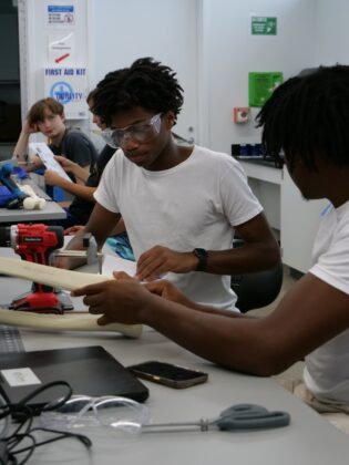 Students collaborate on a hands-on engineering project at Lawrence Tech summer programs, using tools and safety gear in a lab setting.