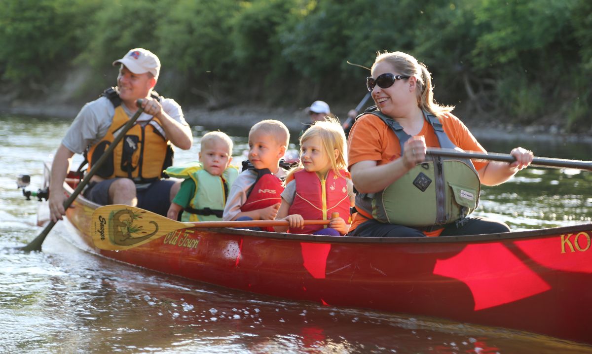Smiling family paddling together in a red canoe on a calm waterway at Indiana Dunes National Park, enjoying a kid-friendly outdoor adventure.