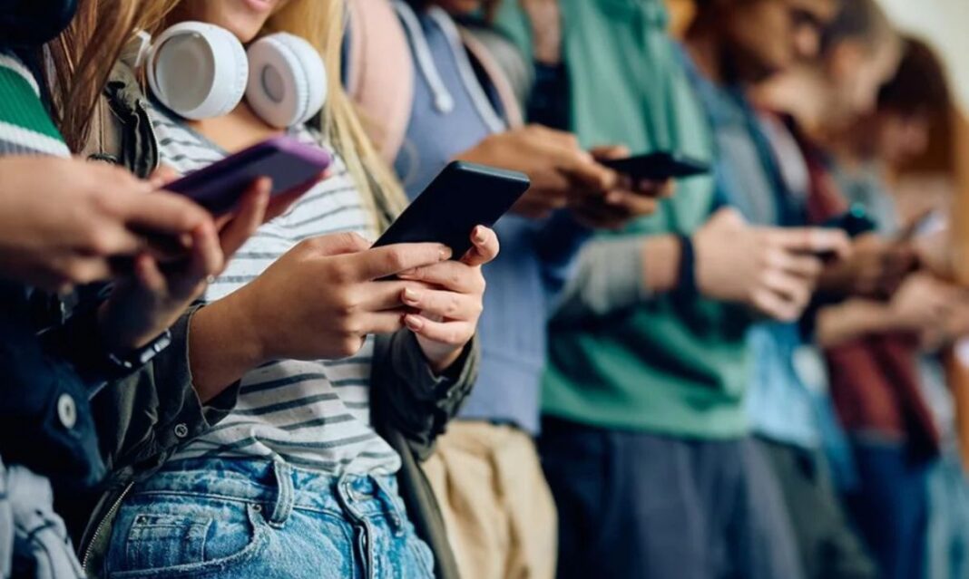 Group of teens using smartphones and texting, representing how kids communicate with internet slang today