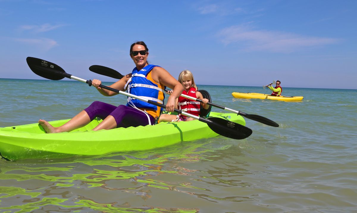 Mom and child kayaking on a sunny lake during a summer family adventure travel road trip with another family member paddling nearby.