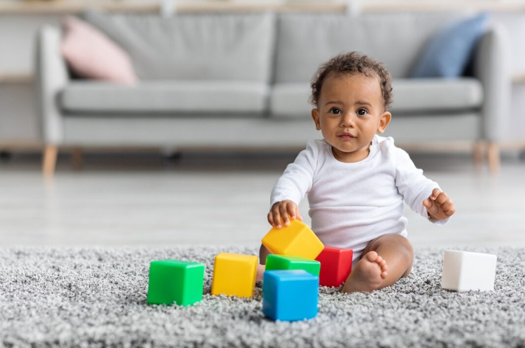 Baby playing with colorful blocks on a carpet, illustrating early childhood development—relevant to LinusBio ClearStrand ASD autism screening.