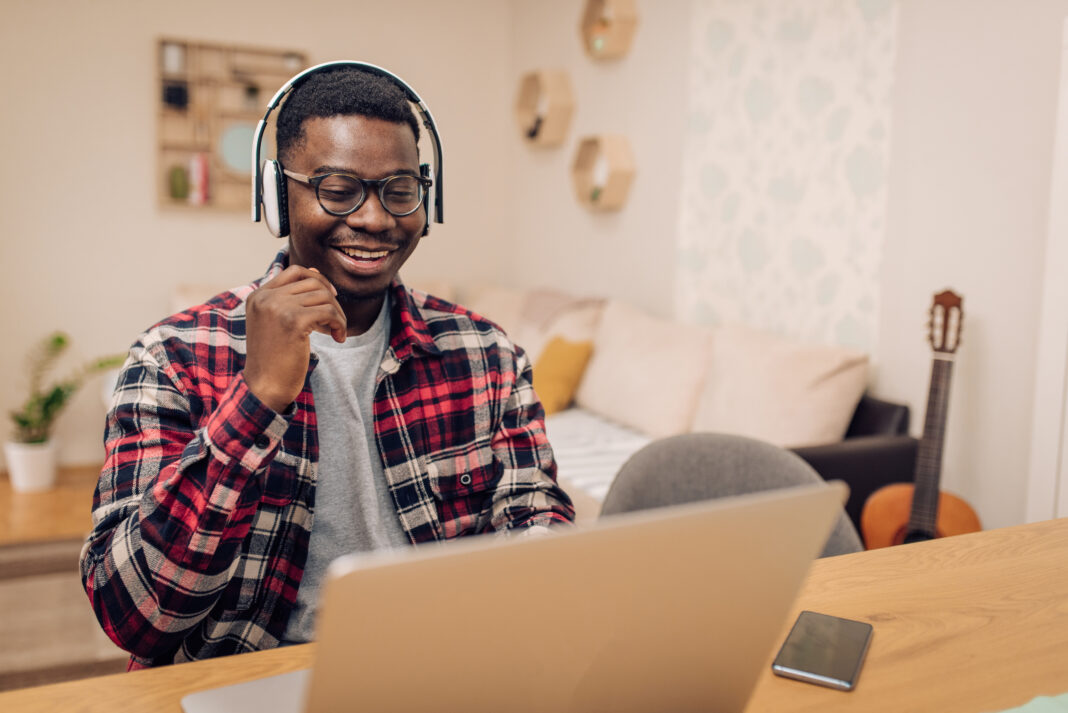Young adult smiling while participating in a virtual MSU Extension Adulting program, wearing headphones and engaging with a laptop from home.