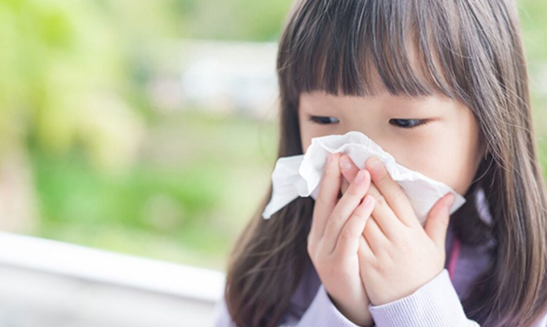 Young girl with seasonal allergies blowing her nose outdoors, showing common allergy symptoms in children.