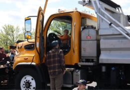 Child sitting in the driver’s seat of a yellow snow plow truck during a Touch-a-Truck community event in Metro Detroit.