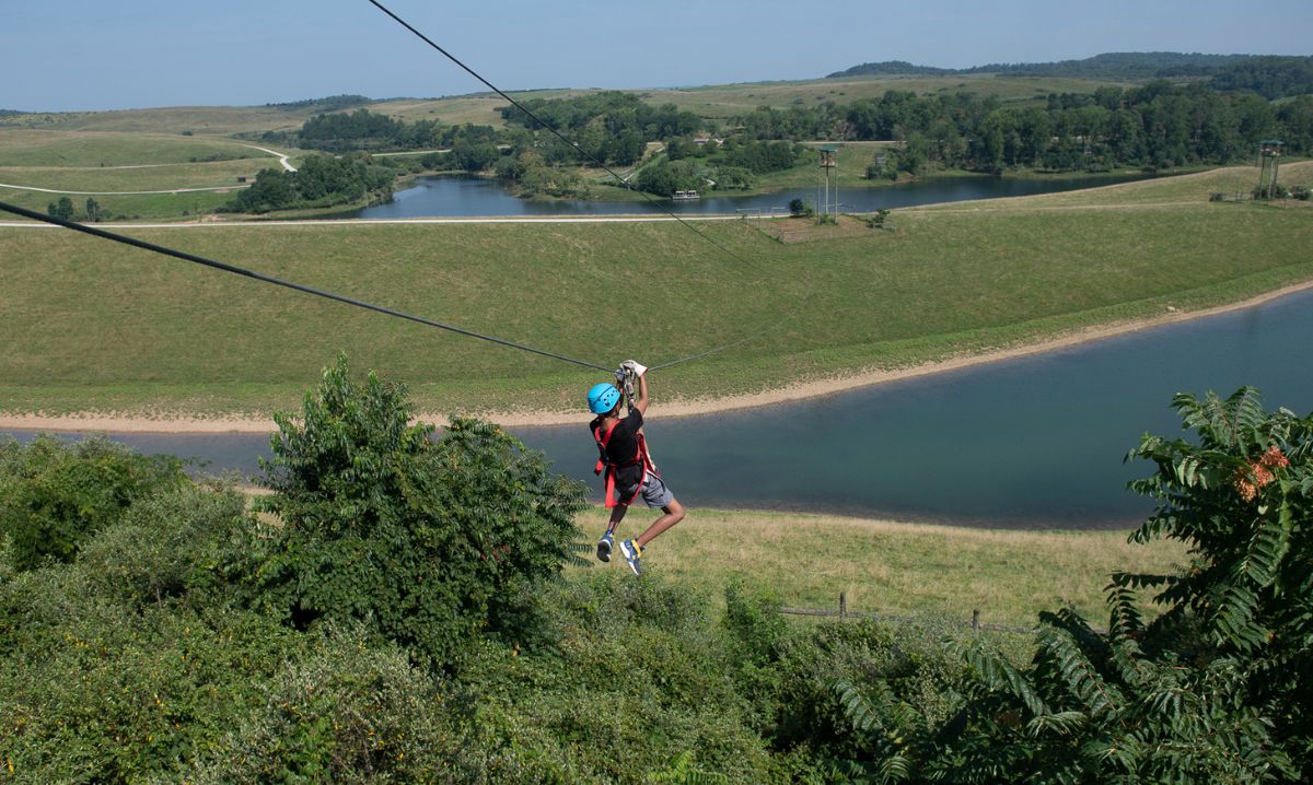 Child ziplining high above scenic lakes and rolling hills at The Wilds in Ohio during an outdoor adventure camp experience.