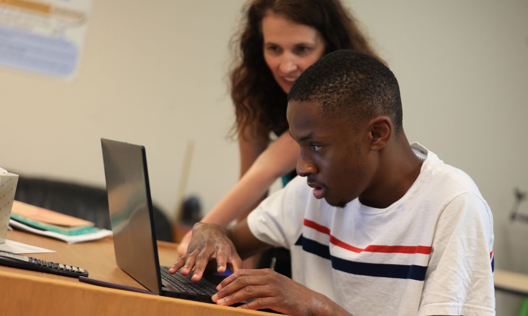 A student at AIM High School in Metro Detroit works on a laptop with guidance from a teacher, highlighting hands-on learning in one of the area's best schools.