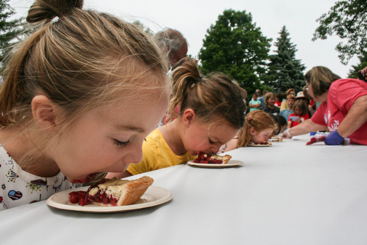 Young girls competing in a cherry pie eating contest at the Traverse City National Cherry Festival, a fun and popular summer event for families in Traverse City.