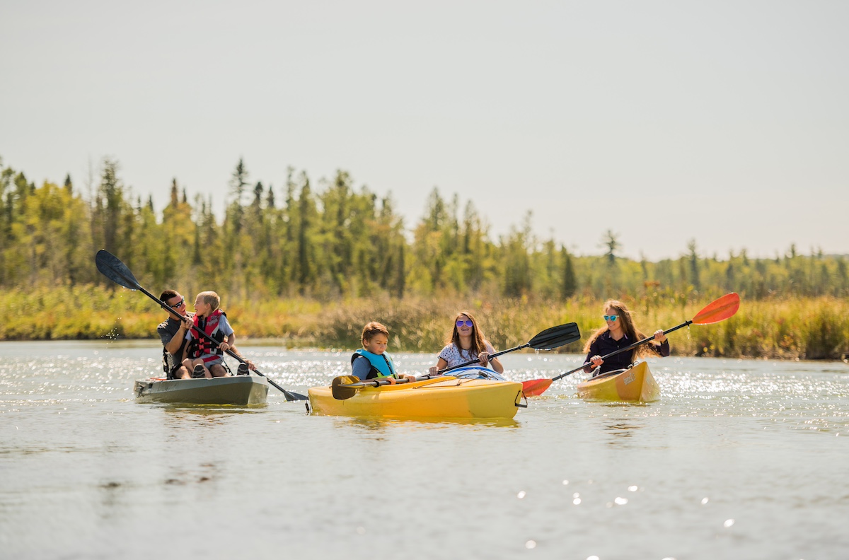 Family kayaking together on a calm river near Traverse City, Michigan, surrounded by forested scenery — one of the top outdoor activities for families visiting Traverse City.