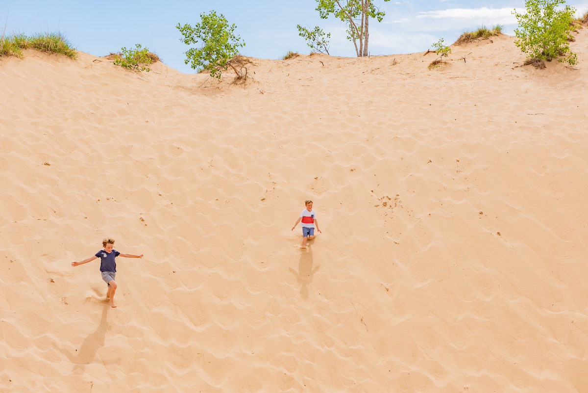 Two kids running down the golden sand at Sleeping Bear Dunes National Lakeshore near Traverse City, Michigan — a fun and adventurous outdoor activity for families visiting the area.