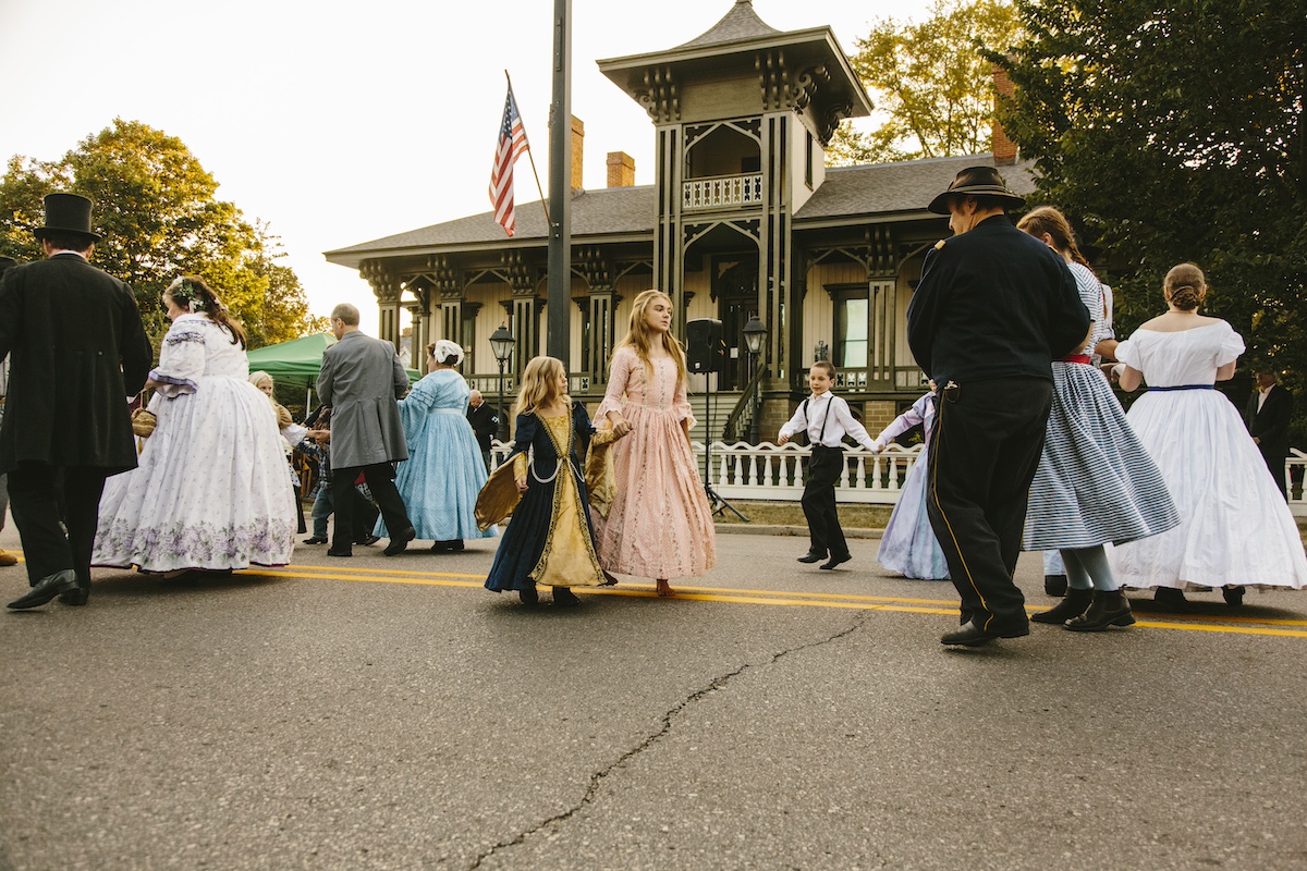 Families dressed in historical costumes participate in a community dance in front of the iconic Honolulu House in the city of Marshall, Michigan — a charming destination full of family-friendly events and history.