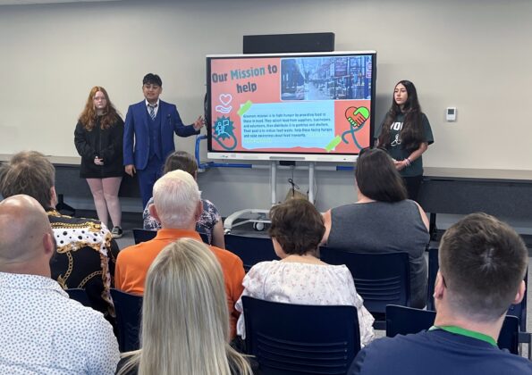 Academy Explorer 6 students present their community project to an audience at Center Line Public Schools, highlighting their mission to fight hunger and reduce food waste.