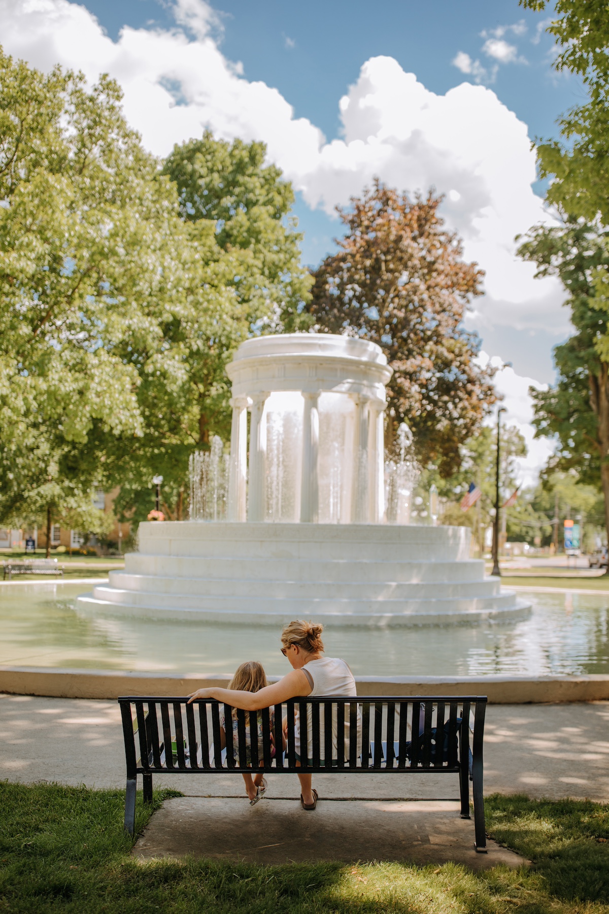 A mother and daughter sit on a bench in front of the historic Brooks Memorial Fountain in the city of Marshall, Michigan — a relaxing and scenic spot for families to enjoy.