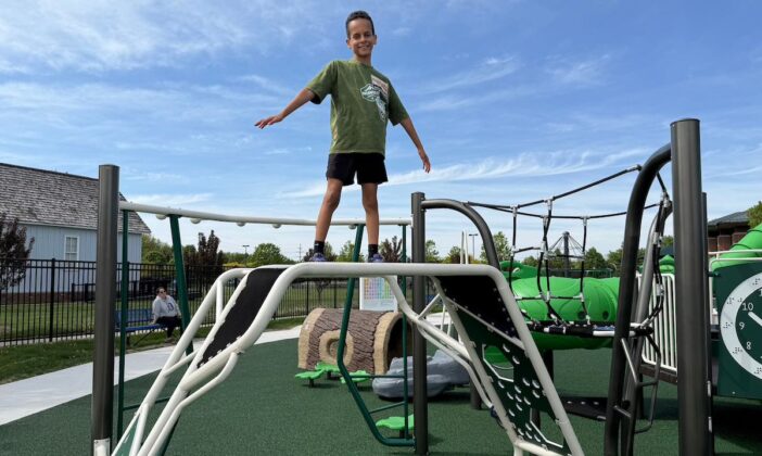 Child balancing on climbing structure at Clinton Township inclusive playground, featuring sensory-friendly and accessible play equipment for kids of all abilities.