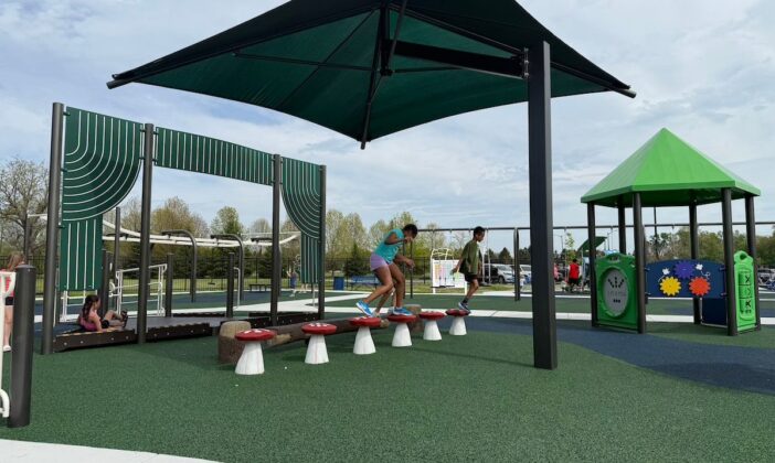Children balance on mushroom-shaped stepping pods at Clinton Township inclusive playground, featuring shaded play areas and accessible equipment for kids of all abilities.