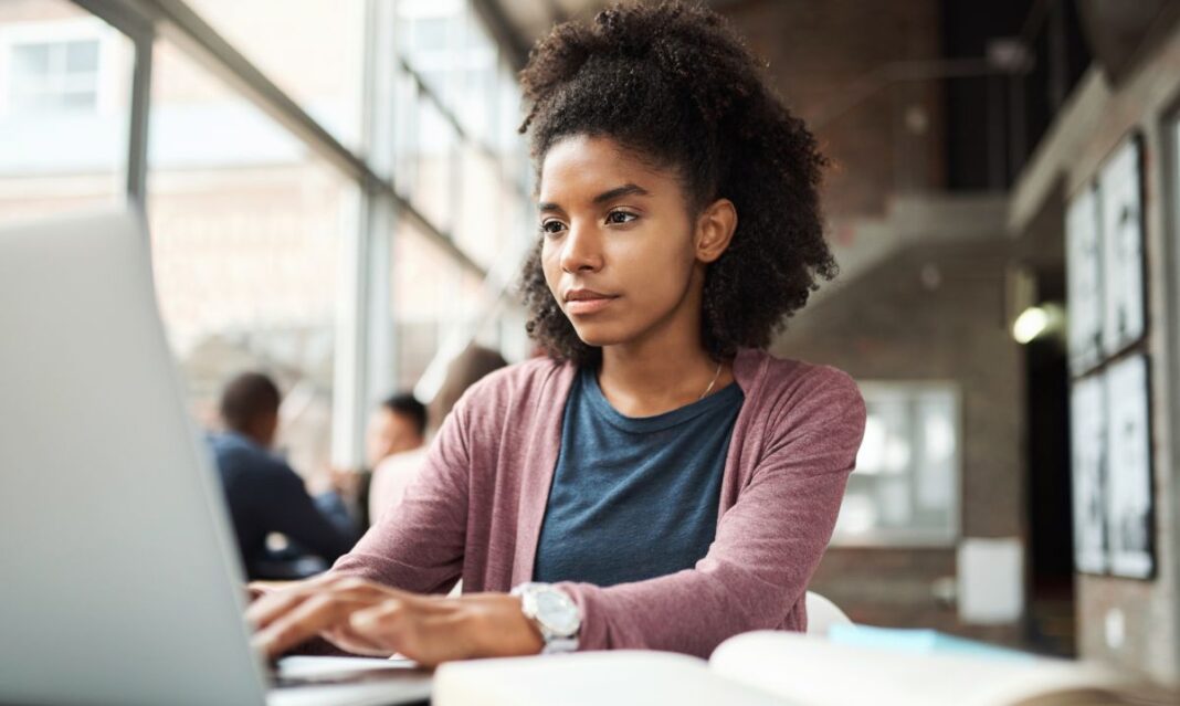 College student working on a laptop in a library or study area, researching how much college costs in Michigan.