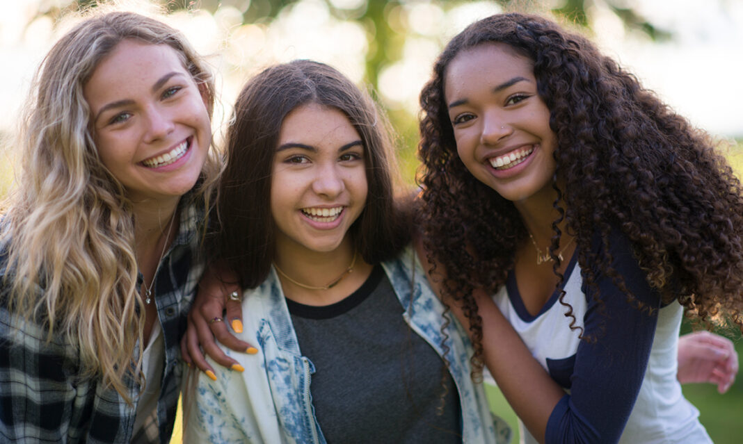Three smiling teen girls enjoying time outdoors in summer, representing friendship, sunshine safety, and teen well-being during school break.