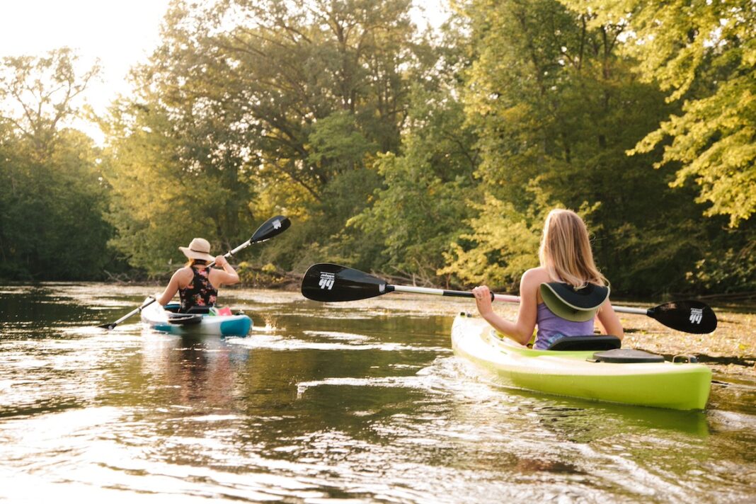 Two women kayaking on a peaceful river in Marshall, one of the top Michigan summer vacation day trip destinations for outdoor lovers