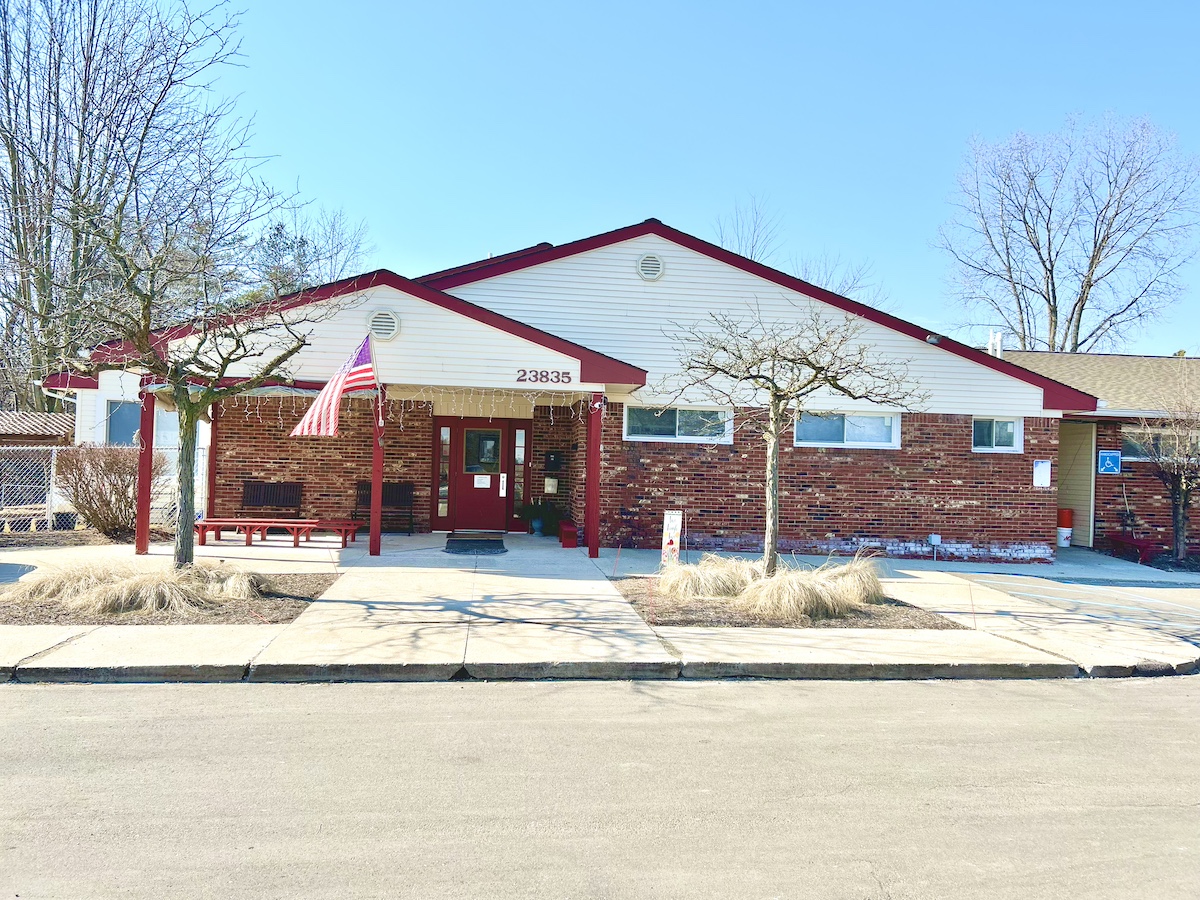 Exterior view of Novi Northville Montessori Center with American flag, red and white trim, and clear blue sky in the background.