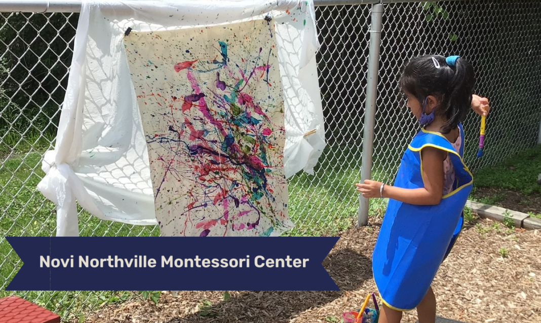 Young girl participates in an outdoor art activity at Novi Northville Montessori Center, painting a large canvas with vibrant splashes of color while wearing a protective smock.