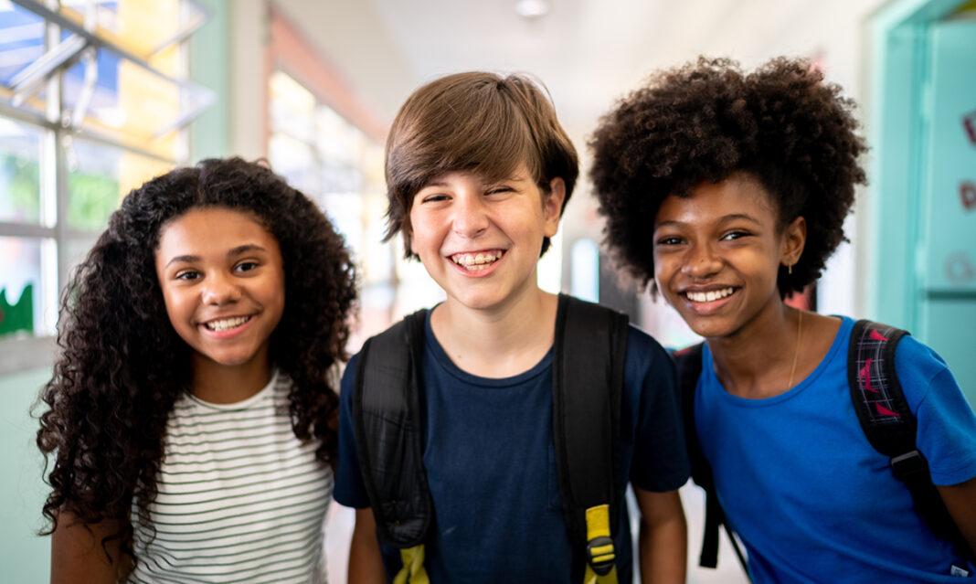 Three middle school students smile in a hallway, representing the need for school mental health support for youth in Oakland County, Michigan.