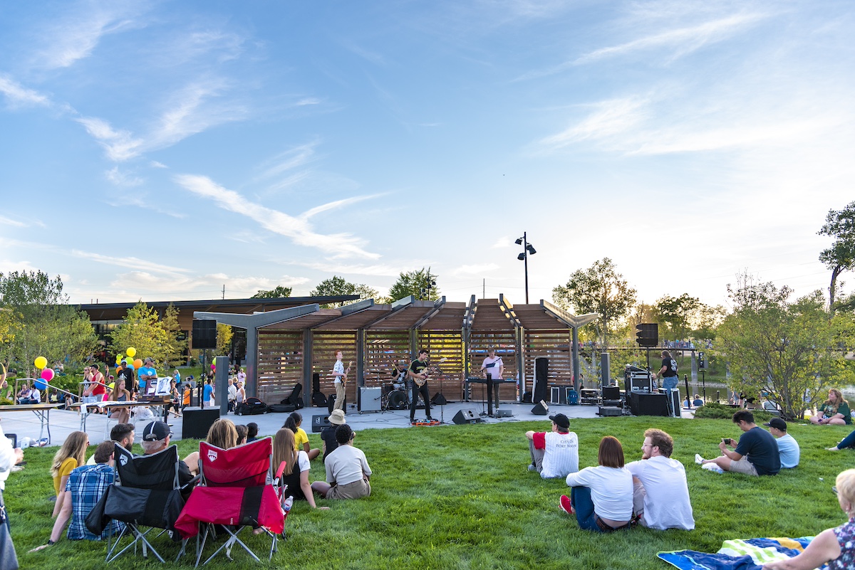 Live music performance at the Sweetwater Band Shell on Auer Lawn in Promenade Park, Fort Wayne, with families and friends relaxing on the grass enjoying the concert.