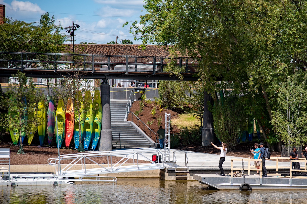 Colorful kayaks lined up near the riverfront with visitors enjoying the floating dock and tree canopy trail at Promenade Park in Fort Wayne, Indiana.