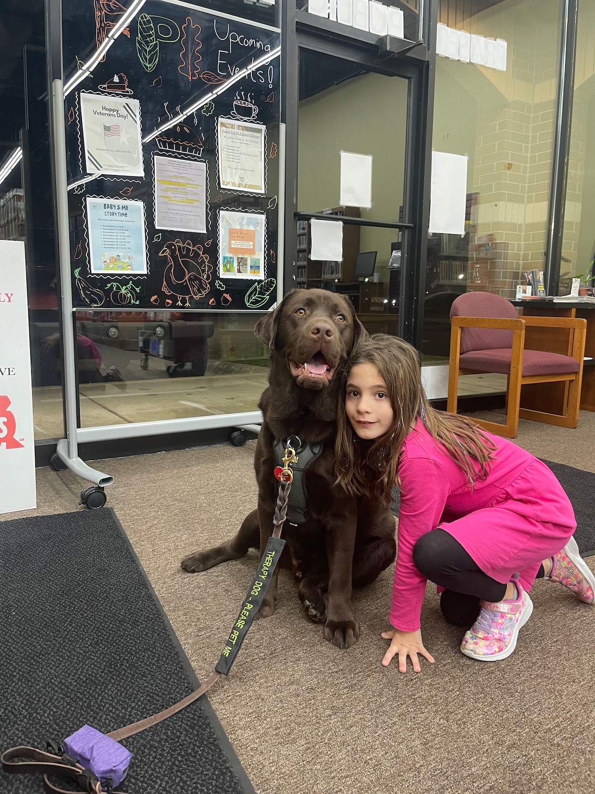 Young girl cuddling a therapy dog at Fraser Public Library during a reading event — one of the best libraries in Macomb County for literacy programs and emotional support experiences for kids.