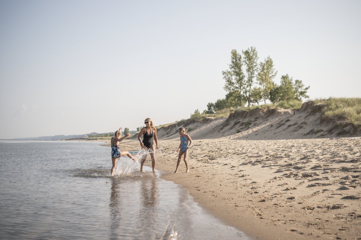 Mom and two young daughters enjoying a sunny beach day on Lake Michigan, one of the best things to do in Saugatuck Michigan with kids.