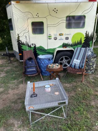 Bronco Wild Fund Days camping trailer with outdoor gear setup, including folding chairs, a grill station, and branded backpacks, promoting nature exploration and conservation.