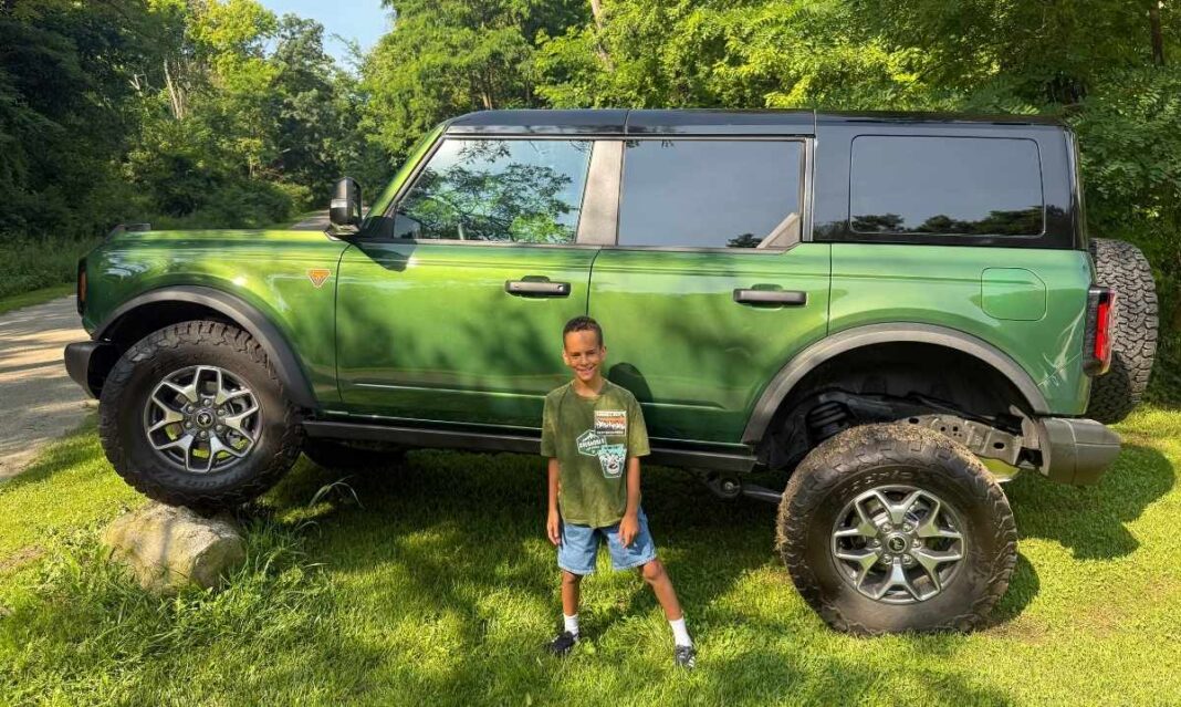 Young boy smiling in front of a green Ford Bronco during Bronco Wild Fund Days, celebrating outdoor adventure and family-friendly off-road experiences.
