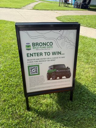 Bronco Wild Fund Days event sign inviting guests to enter for a chance to win a 2025 Ford Bronco Big Bend, set up on a grassy outdoor area.