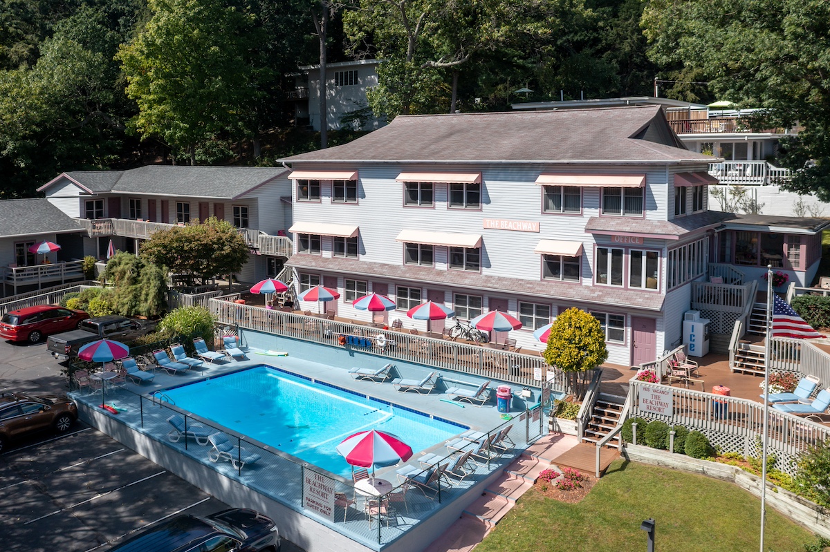 A sunny exterior view of The Beachway Resort, one of the top-rated family hotels in Saugatuck Michigan, featuring a large outdoor pool, colorful umbrellas, and family-friendly accommodations.