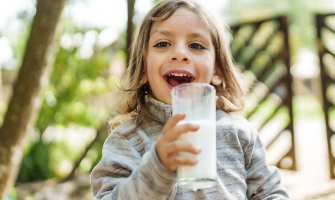 Child in Michigan smiling while drinking a glass of milk, an important source of vitamin D for kids’ healthy growth and strong bones.