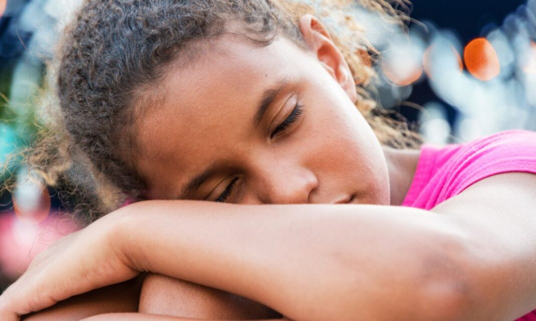 Tired child resting outdoors, showing signs of summer fatigue in kids.