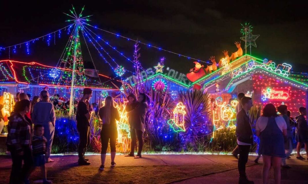Families walking past houses covered in colorful Christmas lights, representing the best holiday light displays in metro Detroit for 2025.