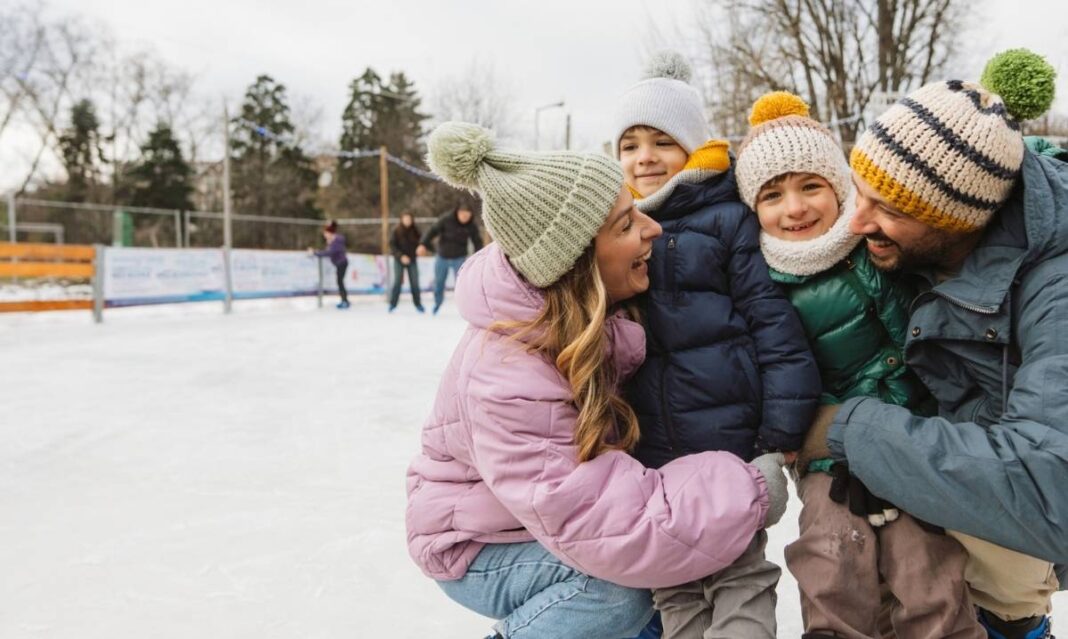 Family smiling together on an outdoor ice rink wearing winter hats and jackets, representing the best outdoor ice skating rinks in metro Detroit.