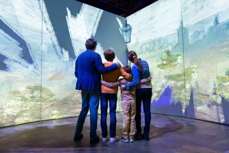 A family explores the Beyond Van Gogh and Beyond Monet immersive exhibit in Detroit surrounded by vibrant projected artwork.