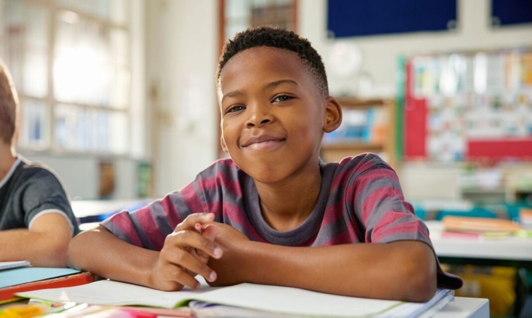 Smiling elementary student sits at his desk in class representing school health tips for parents to support learning and well-being.