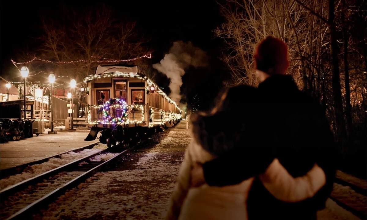 Couple watches the festive Huckleberry Railroad train decorated with Christmas lights at Crossroads Village in Flint during the holiday season.
