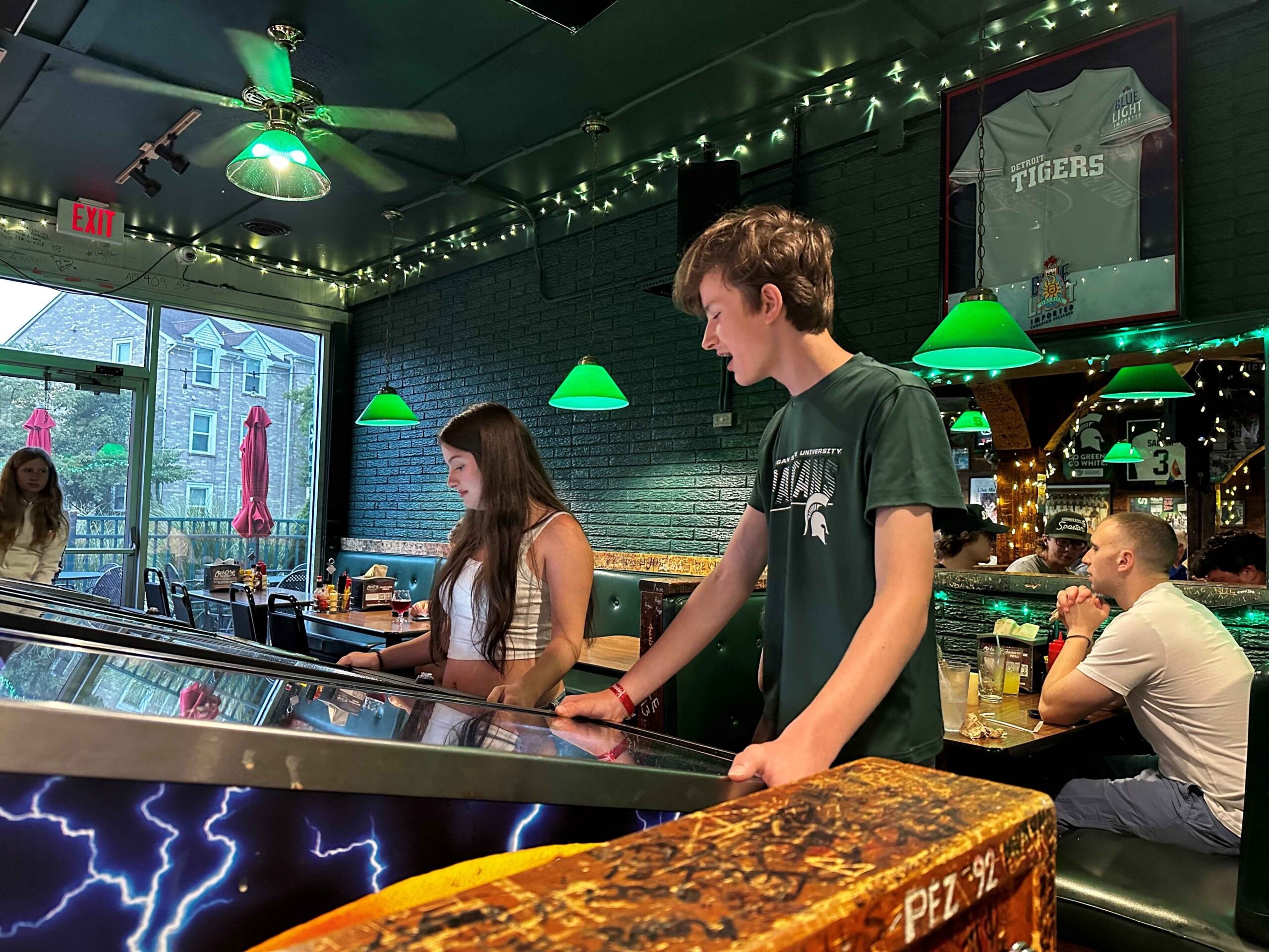 Teens enjoy playing pinball at Crunchy’s in Lansing while diners relax in booths, highlighting the restaurant’s fun and casual vibe.
